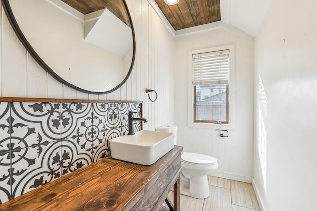 half bathroom with vaulted ceiling, toilet, and a sink