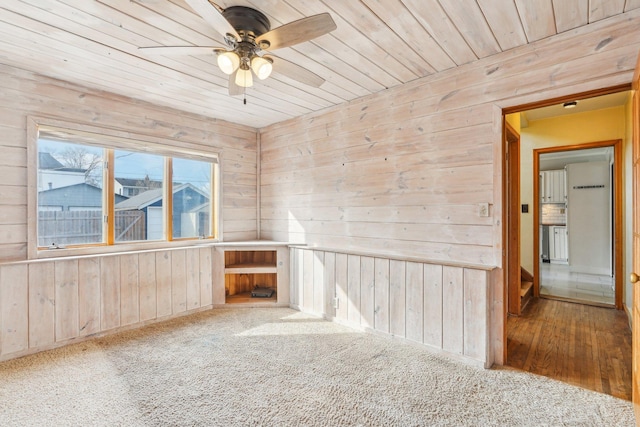 spare room with carpet flooring, wood walls, wooden ceiling, and a ceiling fan