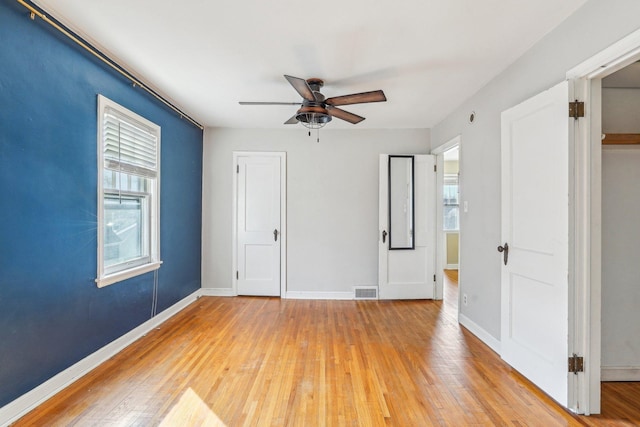 empty room featuring a wealth of natural light, baseboards, light wood-style floors, and ceiling fan