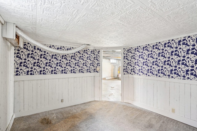 spare room with carpet floors, wooden walls, an ornate ceiling, and wainscoting