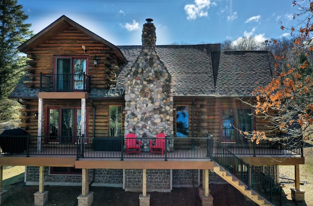 rear view of property with log siding, a balcony, a chimney, and roof with shingles