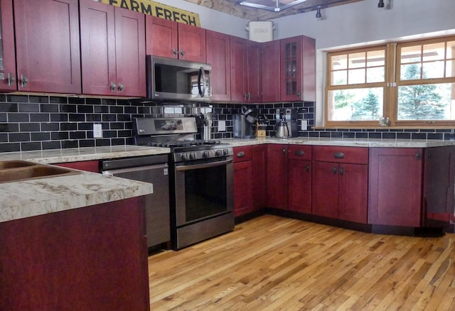 kitchen with light wood-type flooring, stainless steel appliances, reddish brown cabinets, and backsplash