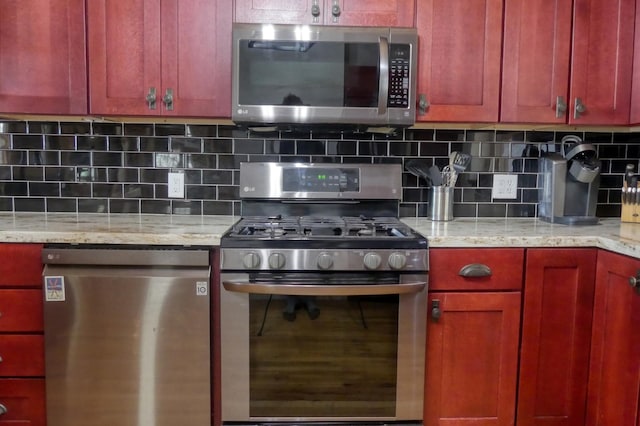 kitchen with tasteful backsplash, appliances with stainless steel finishes, light stone counters, and reddish brown cabinets