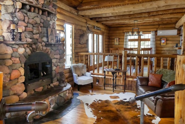 living room featuring a wall unit AC, beam ceiling, a stone fireplace, hardwood / wood-style flooring, and a notable chandelier