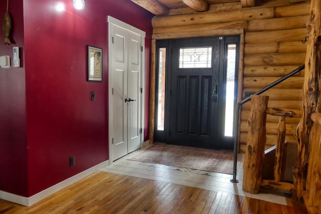 foyer entrance with rustic walls, beamed ceiling, baseboards, and hardwood / wood-style floors