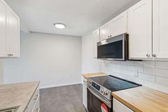 kitchen featuring decorative backsplash, white cabinets, stainless steel appliances, and baseboards