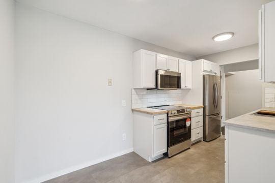 kitchen featuring tasteful backsplash, baseboards, light countertops, white cabinets, and stainless steel appliances