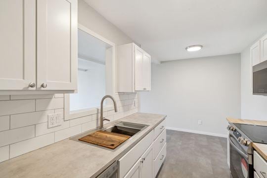 kitchen with baseboards, stainless steel electric stove, a sink, white cabinetry, and backsplash