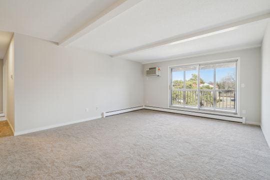 empty room featuring a wall mounted air conditioner, a baseboard heating unit, beam ceiling, and carpet floors