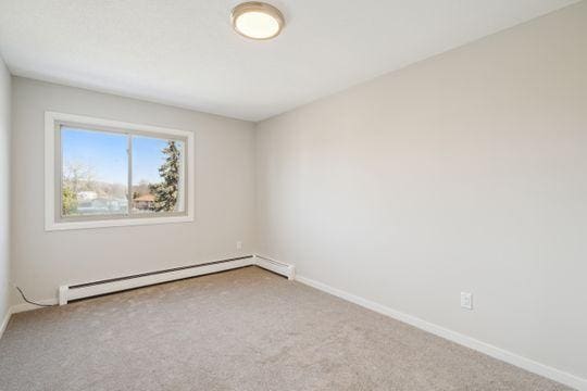 carpeted spare room featuring a baseboard heating unit and baseboards