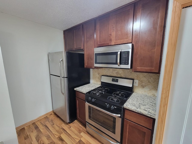 kitchen featuring tasteful backsplash, baseboards, light wood-type flooring, stainless steel appliances, and a textured ceiling