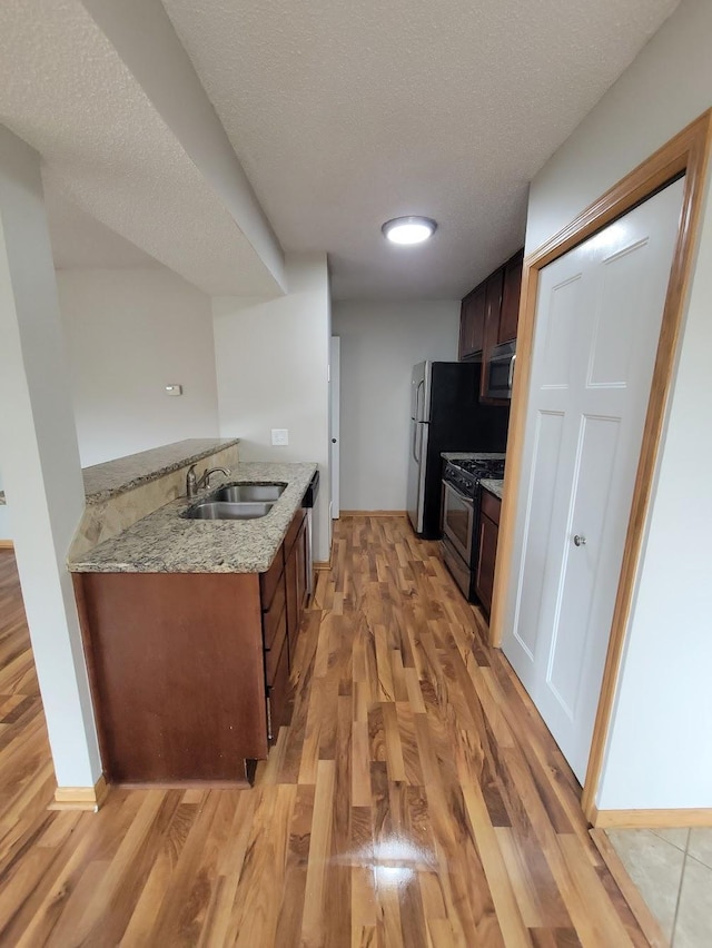 kitchen with light wood-style flooring, a sink, a textured ceiling, stainless steel appliances, and baseboards