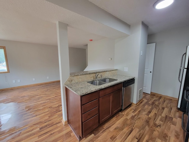 kitchen with a sink, light stone countertops, light wood-type flooring, refrigerator, and stainless steel dishwasher