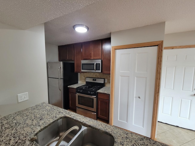 kitchen with light stone countertops, light tile patterned flooring, a sink, stainless steel appliances, and a textured ceiling