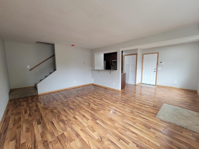 unfurnished living room with stairs, baseboards, light wood finished floors, and a textured ceiling