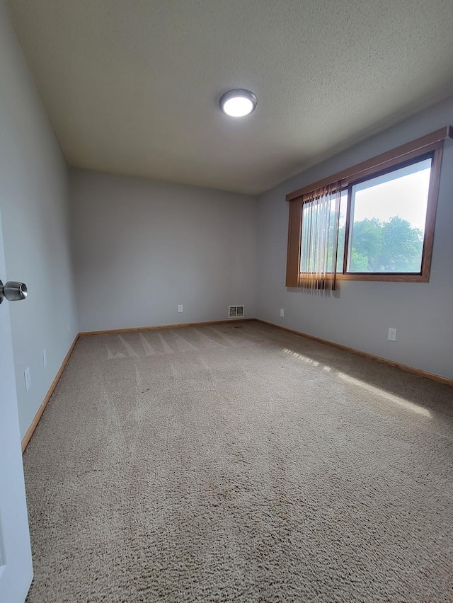 spare room with visible vents, light colored carpet, a textured ceiling, and baseboards