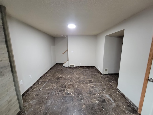 finished below grade area featuring visible vents, baseboards, a textured ceiling, and stairs