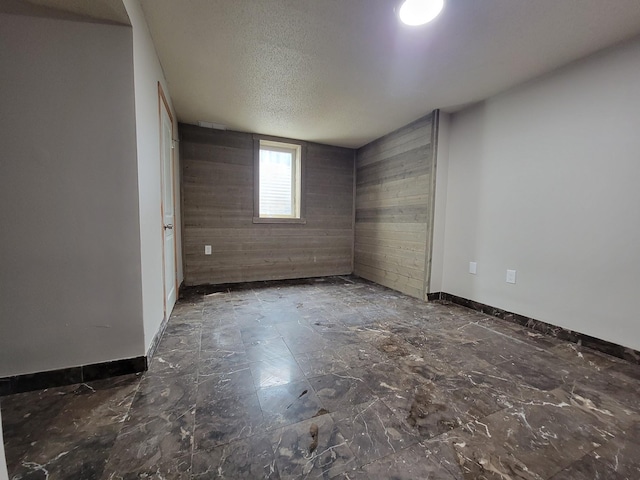 unfurnished room featuring wooden walls, a textured ceiling, and baseboards