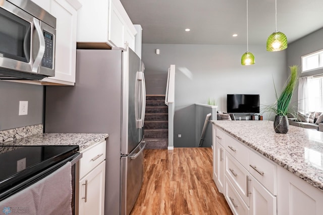 kitchen with decorative light fixtures, stainless steel appliances, light wood-style floors, white cabinets, and light stone countertops