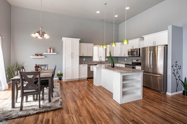 kitchen with open shelves, a high ceiling, a sink, appliances with stainless steel finishes, and a center island