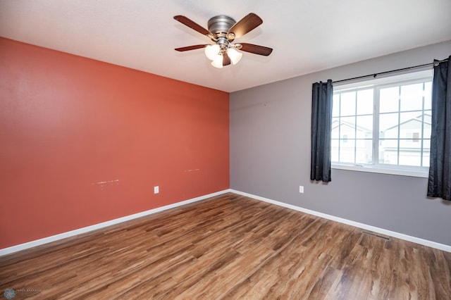 unfurnished room with ceiling fan, visible vents, baseboards, and wood finished floors