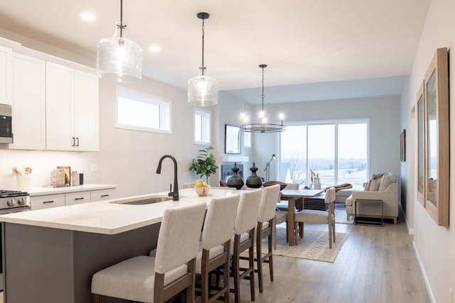 kitchen with light wood-style flooring, a kitchen island with sink, a sink, light countertops, and appliances with stainless steel finishes