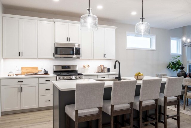 kitchen with a center island with sink, a sink, light wood-style floors, appliances with stainless steel finishes, and light countertops