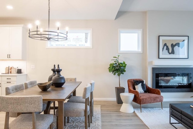 dining area featuring a chandelier, a glass covered fireplace, light wood-style flooring, and baseboards