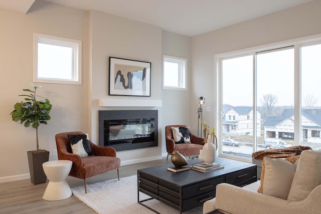 sitting room featuring a glass covered fireplace, baseboards, and wood finished floors