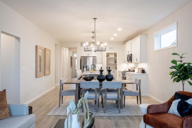 dining area with an inviting chandelier, light wood-style floors, baseboards, and visible vents