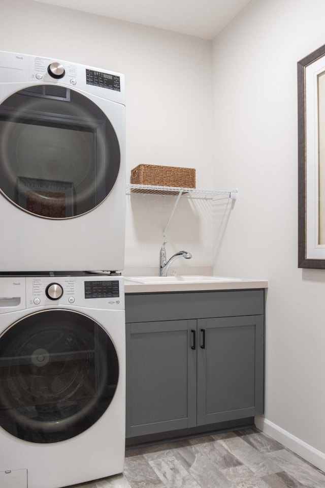 clothes washing area featuring baseboards, cabinet space, stacked washer and clothes dryer, and a sink