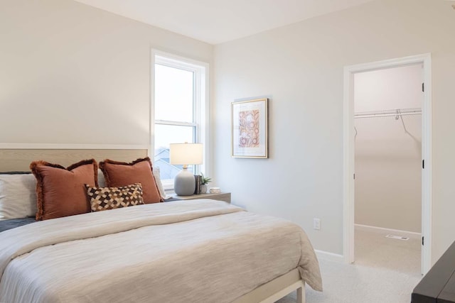 bedroom with a walk in closet, light colored carpet, baseboards, and a closet