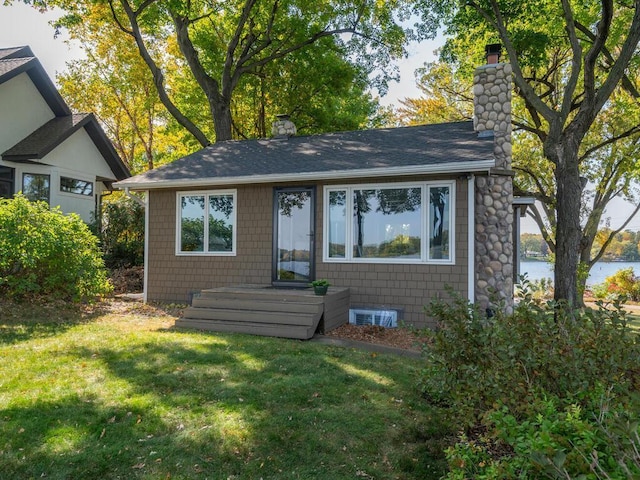 view of front of home featuring a chimney, roof with shingles, a front yard, and a water view