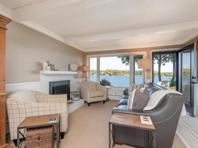 carpeted living room with beamed ceiling, a fireplace with raised hearth, a water view, and a textured ceiling