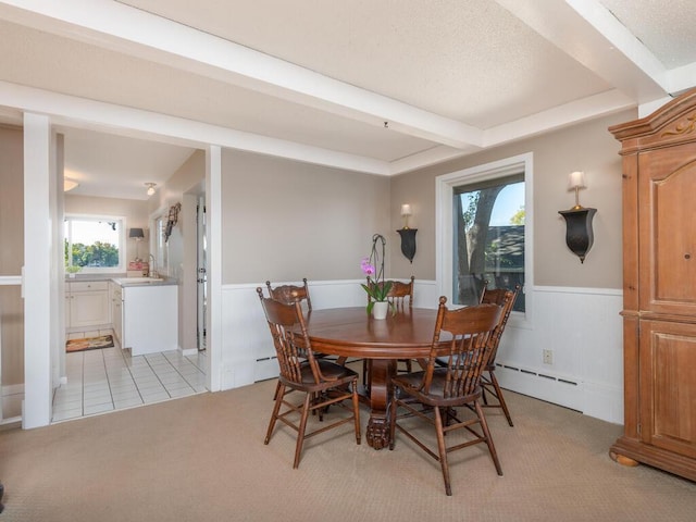 dining area with wainscoting, a baseboard heating unit, beamed ceiling, light colored carpet, and baseboard heating