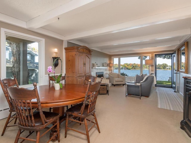 dining space with beam ceiling, light colored carpet, a fireplace, and a water view