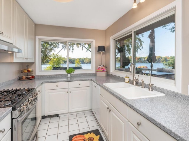 kitchen featuring stainless steel gas stove, a sink, under cabinet range hood, white cabinets, and light tile patterned floors