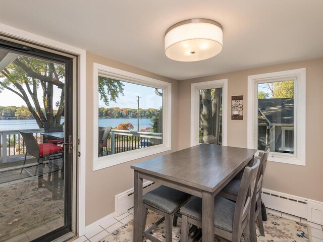 dining space with baseboards, a water view, baseboard heating, and light tile patterned flooring