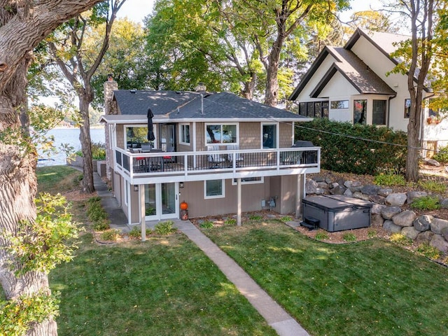 rear view of house with a yard, a deck with water view, a chimney, and a hot tub