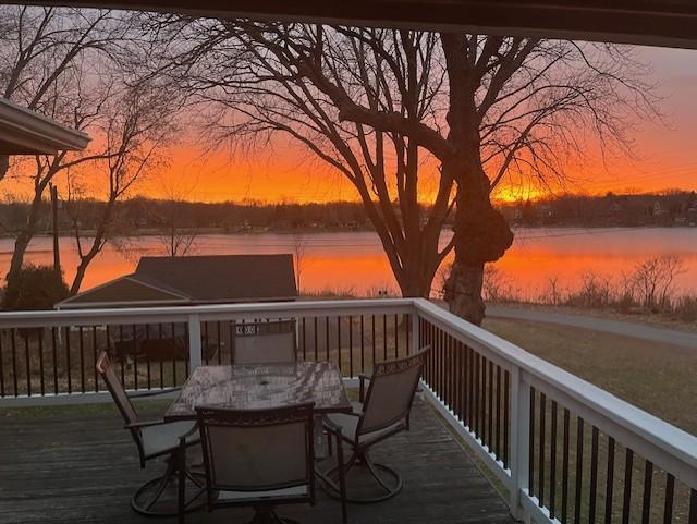 deck at dusk with outdoor dining area and a water view