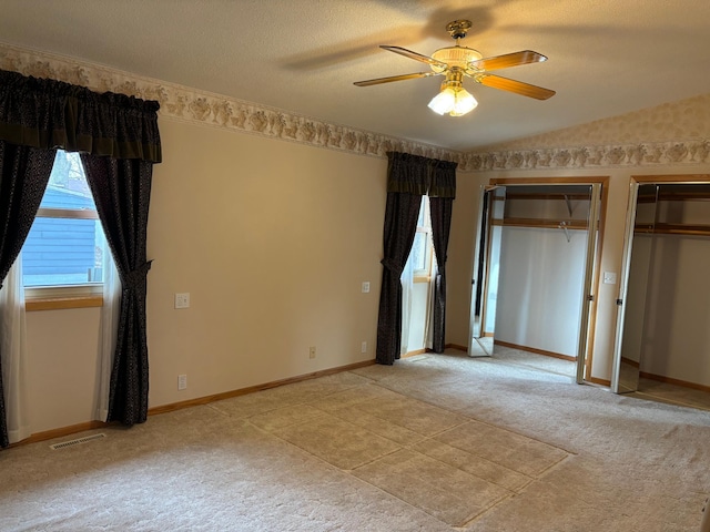 unfurnished bedroom featuring visible vents, multiple closets, a ceiling fan, baseboards, and vaulted ceiling