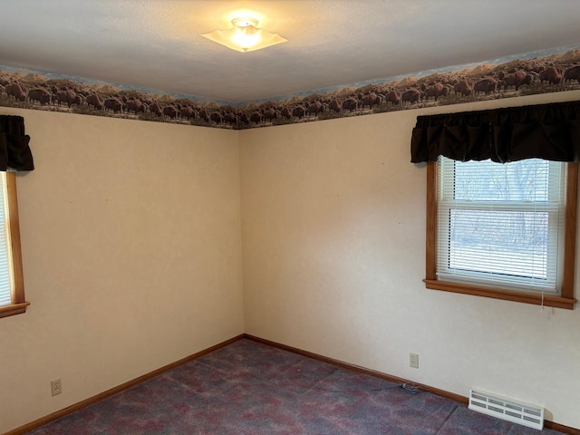 spare room featuring baseboards, visible vents, and dark carpet