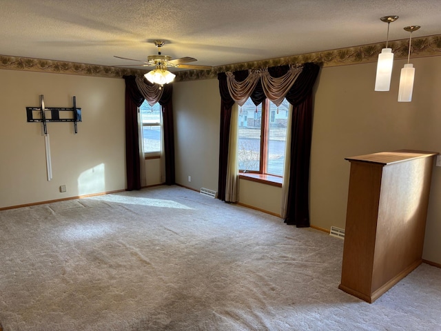 spare room featuring light colored carpet, a textured ceiling, baseboards, and a ceiling fan