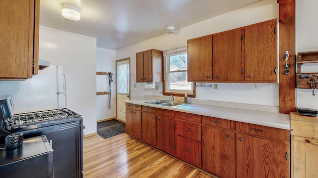 kitchen featuring light wood-style flooring, freestanding refrigerator, a sink, light countertops, and gas range