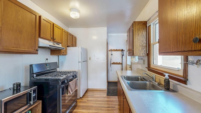 kitchen with brown cabinetry, a sink, black range with gas cooktop, under cabinet range hood, and stainless steel microwave