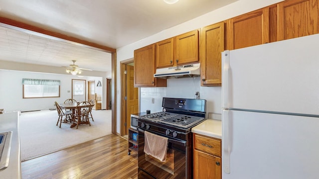 kitchen with brown cabinetry, light wood finished floors, black gas stove, freestanding refrigerator, and under cabinet range hood