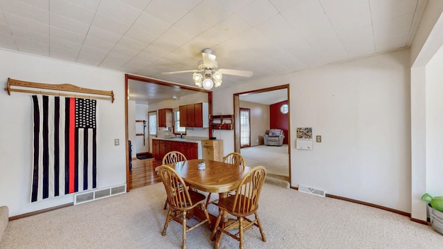 carpeted dining room featuring a sink, visible vents, baseboards, and ceiling fan