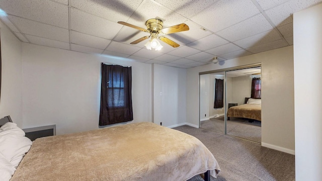 carpeted bedroom with a closet, a drop ceiling, a ceiling fan, and baseboards