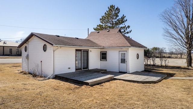 back of house featuring a lawn, a wooden deck, and roof with shingles