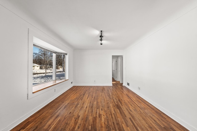 unfurnished room with track lighting, wood finished floors, and baseboards